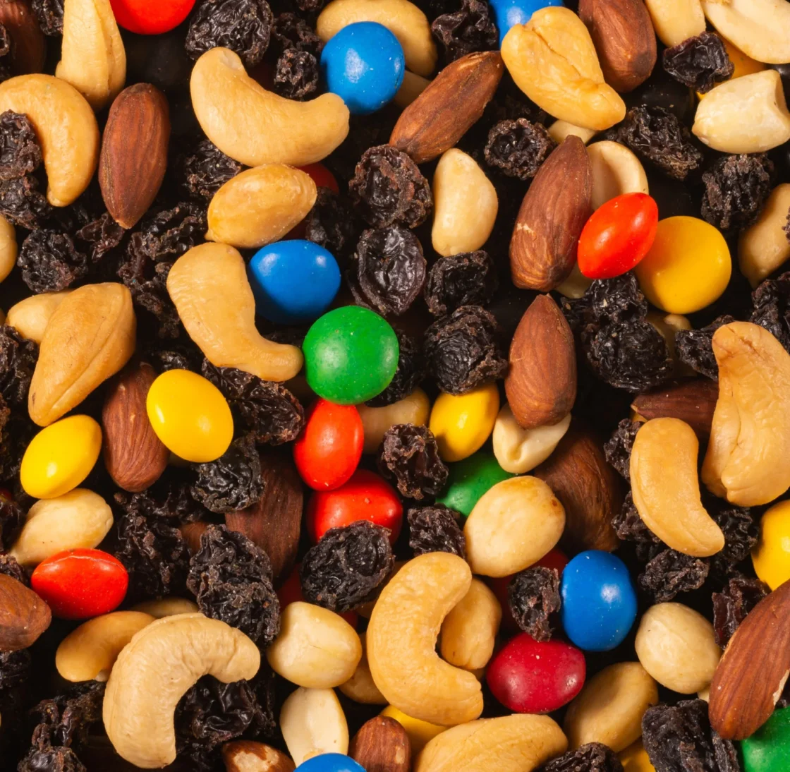 Bulk trail mix featuring cashews, almonds, raisins, and colorful candies for wholesale food distribution and foodservice supply.